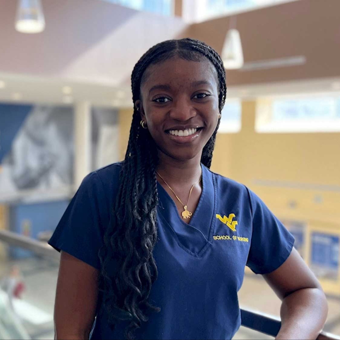 Selasi Asamoah wears dark blue scrubs with a gold Flying WV School of Nursing logo.